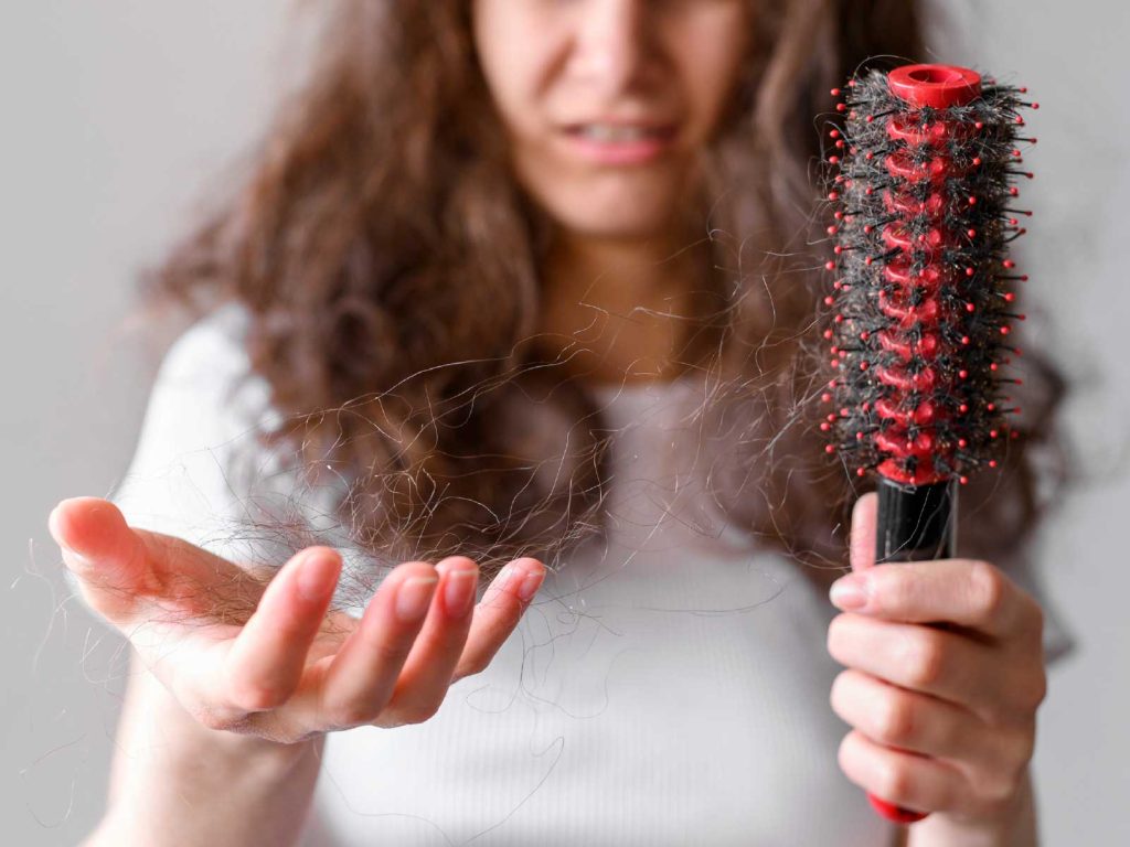 Mulher com cabelo caindo junto à escova de cabelo.